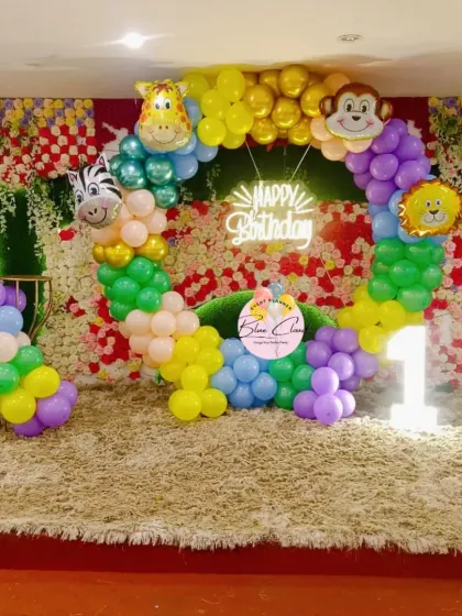 A fun safari-themed first birthday stage setup with a balloon ring, animal foils, and a light-up number '1'.
