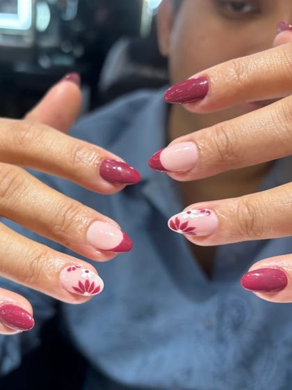A modern and chic nail art design featuring a deep berry color. The look is balanced with negative space and simple floral accents for a sophisticated yet artistic manicure.