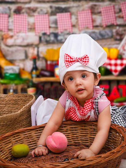 A curious little chef exploring her surroundings. The rustic brick background and picnic basket add to the charm of this kitchen-themed shoot.