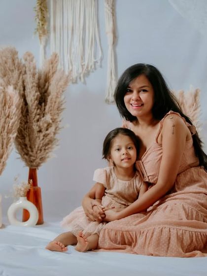 A classic seated portrait from the boho-themed Mom & Me session. Their coordinated outfits and the beautifully decorated set create a stunning and memorable photograph.