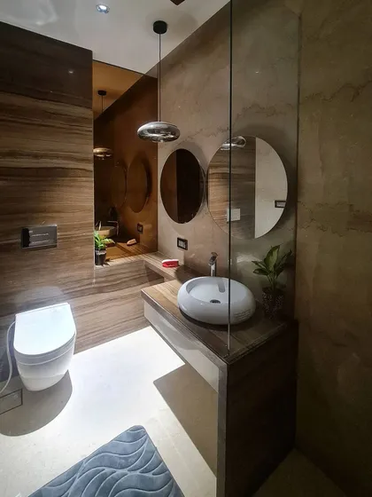 This washroom achieves a warm, monolithic look using travertine-style marble throughout the walls and vanity. The space is accented with a modern chrome pendant light and a vessel sink, creating a practical yet opulent interior.