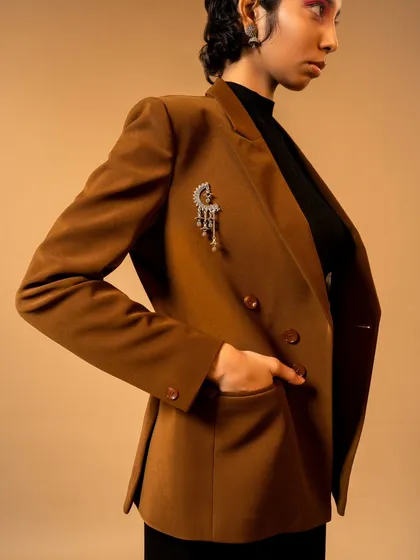 A detail-oriented shot focusing on a tailored brown blazer with a unique brooch. The composition is clean and commercial, perfect for a product-focused lookbook.
