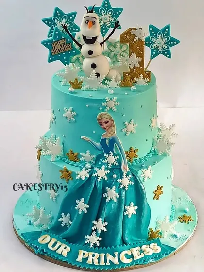A captivating two-tier Frozen-themed cake. This design features a fondant Elsa whose dress flows down the cake, along with Olaf on top and numerous snowflake decorations.