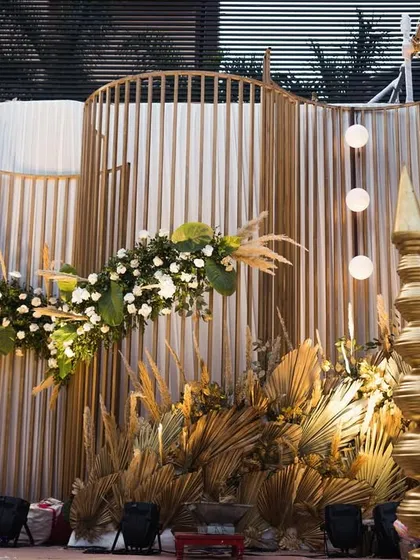 The modern mandap setup, featuring a curved backdrop and dramatic lighting. The golden hues of the dried foliage create a warm and inviting glow.