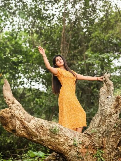 A candid, joyful moment captured in nature. The model is standing on a tree trunk, expressing a sense of freedom and connection with the environment.