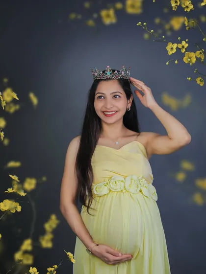 Every mother is a queen. This beautiful studio portrait captures a smiling mom-to-be in a soft yellow dress, adjusting her crown with a gentle touch.
