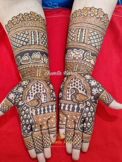 This full-hand baby shower design combines traditional mehendi art with personal touches. The forearms feature bands with baby toys and rattles, while the palms showcase classic peacock motifs within architectural jharokha frames.