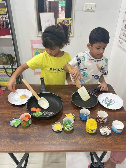 Two young learners engaged in our cooking role-play activity. This kind of play helps develop sequencing skills, vocabulary related to food and actions, and cooperative social skills.