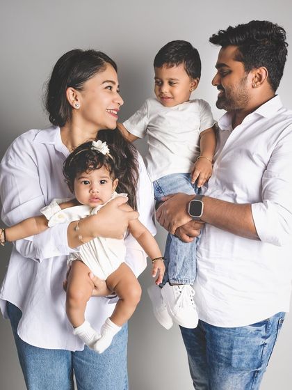 A candid and happy studio portrait of a family of four. The parents hold their two young children, all sharing a moment of connection and joy.
