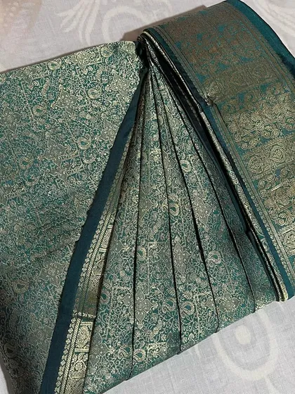 A deep green brocade saree, folded to protect its intricate weaving.