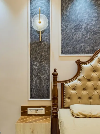 A close-up of the bedside area, showing the classic carved bedpost, the textured wall finish, and the modern wall lamp. This mix of styles creates a unique and eclectic look.