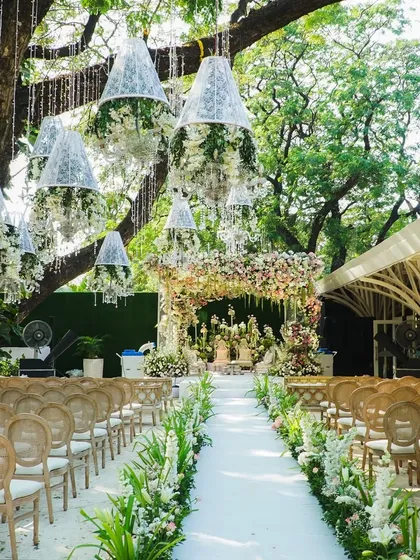 The wedding aisle, lined with lush greenery and with floral chandeliers hanging from the trees, created an enchanted garden path leading to a fairytale mandap.