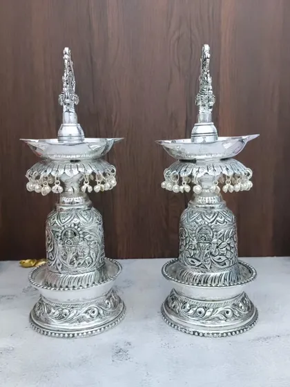German silver se bane yeh Hamsa designer diya ka joda aapke pooja ghar ki shobha badha dega. Inka antique finish aur neeche lage moti inhein ek royal look dete hain.