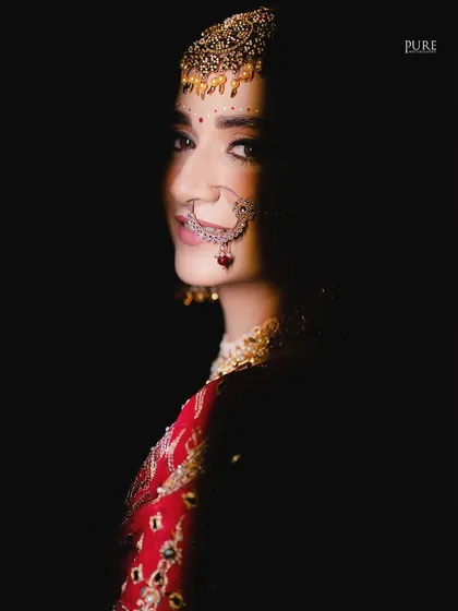 An artistic shot using shadow to create a sense of mystery and elegance. Only half of the bride's face is lit, drawing attention to her eyes and nath.