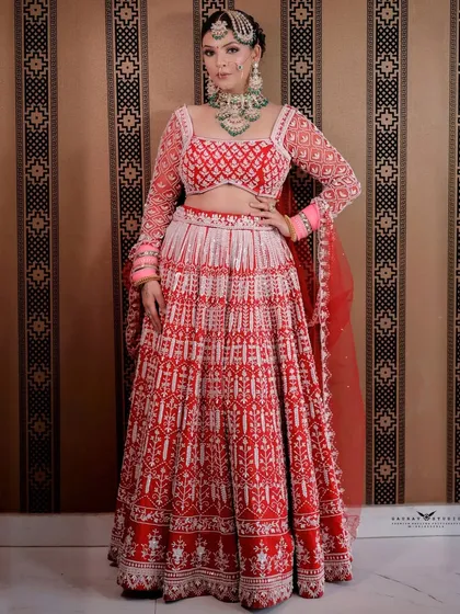 A full-length portrait showcasing the unique red and white patterned lehenga against a complementary striped wall.