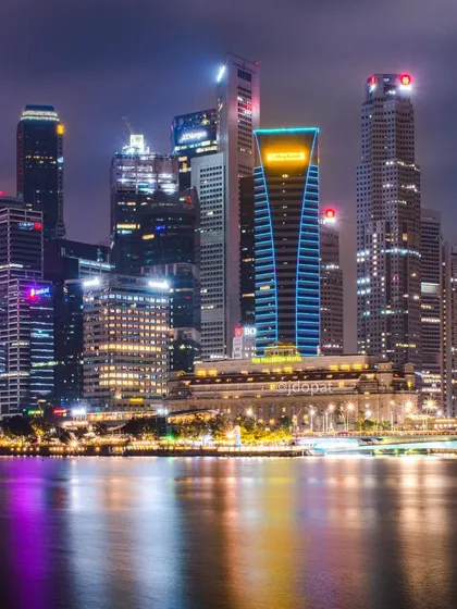 A stunning night photograph of Singapore's skyline, with the colorful lights of the skyscrapers reflecting in the dark water.