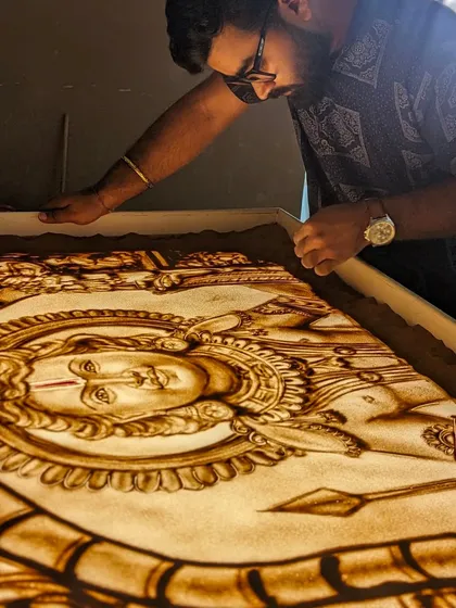 The final touches on a large-scale sand art piece. The light from the lightbox illuminates the sand, giving it a divine glow.