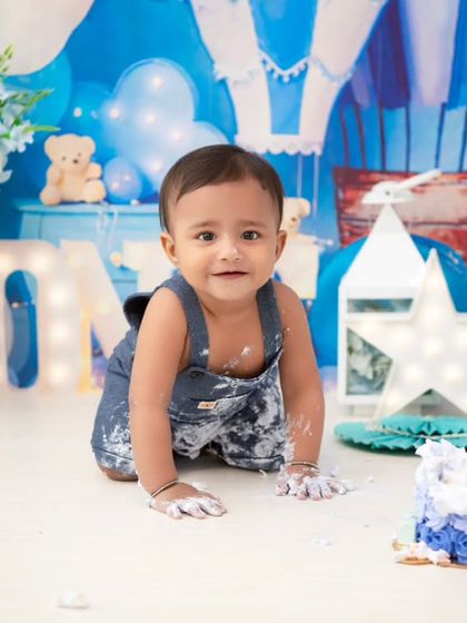 A messy and happy cake smash moment. The blue hot air balloon theme is a popular choice for boys, and the cake-covered hands and face are a sign of a successful session!