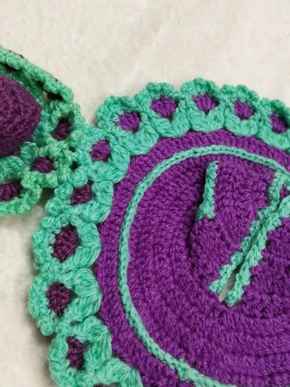 A close-up of the matching cap for the purple and green woolen dress. It's designed to fit comfortably and keep Bal Gopal warm.