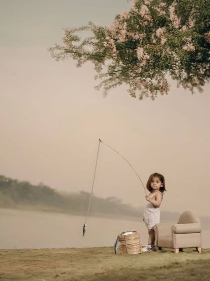 A creative portrait of a little girl pretending to fish by a serene, misty lake. The soft light and charming props create a timeless and imaginative scene that captures the playful spirit of childhood.