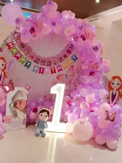 A magical fairy-themed first birthday party. This decoration features a balloon arch in shades of pink and purple, fairy cutouts, a personalized photo display, and a light-up number '1' to mark the special milestone.