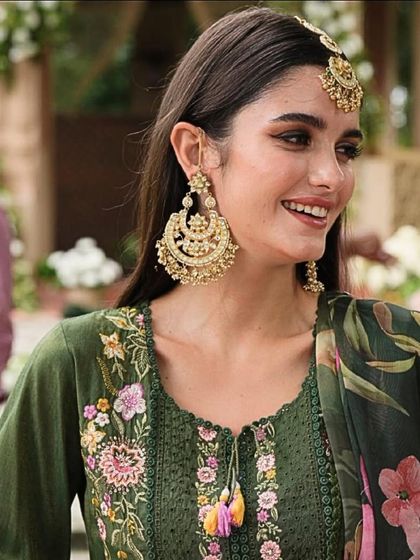 A candid shot of a model smiling, wearing large gold chandbali earrings and a matching maang tikka. These are perfect for a sangeet or mehendi look.