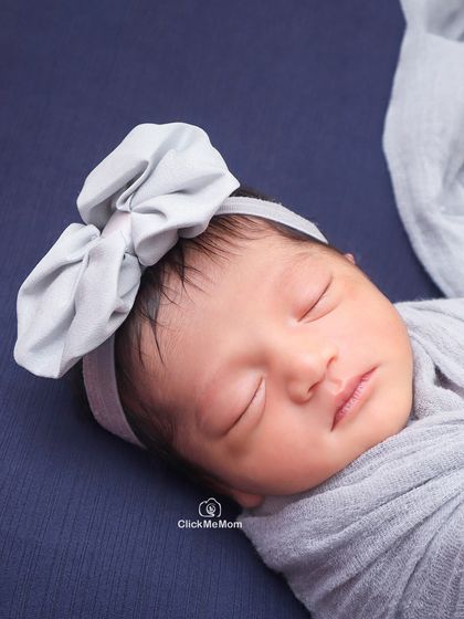 A serene close-up of a sleeping newborn. The simple gray bow and swaddle draw all the attention to her peaceful and perfect features.