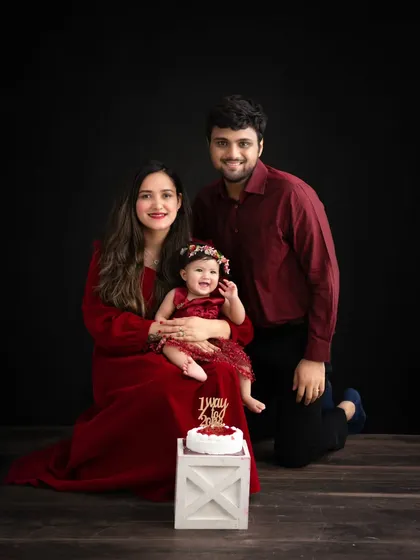A rich and elegant family portrait. The family's coordinated deep red outfits against a dark backdrop create a dramatic and timeless feel, perfect for a milestone celebration.