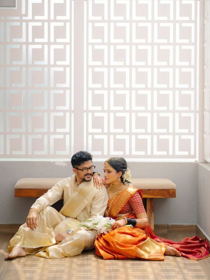 A romantic shot of Archana and her partner. Her orange Kanjeevaram and embroidered blouse create a stunning visual against the modern, minimalist background.