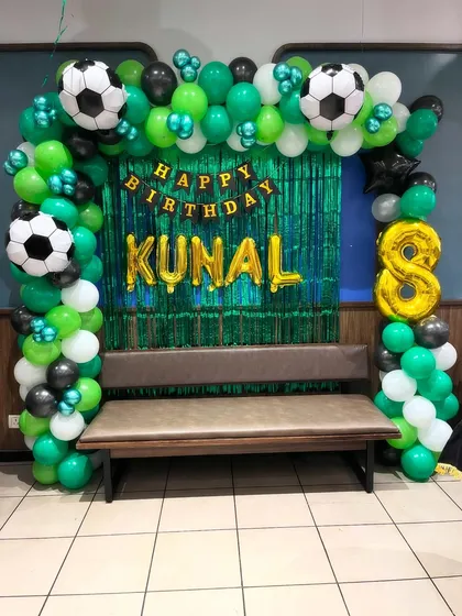 A football-themed birthday decoration for an 8-year-old. This setup includes a balloon arch in green, black, and white, a shimmering green foil curtain, and football-shaped balloons to complete the sporty look.