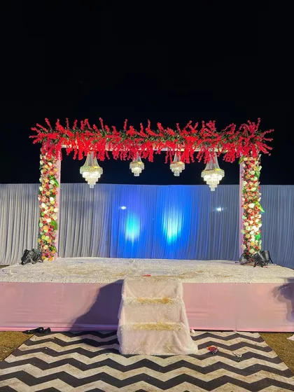 A simple yet striking stage design with a bold red floral header. The hanging crystal chandeliers add a touch of glamour against the simple blue-lit backdrop.