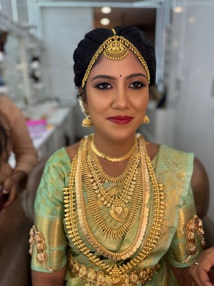 A close-up of my beautiful bride Harina's traditional Muhurtham look. Her makeup features a classic winged eyeliner and a bold red lip, perfectly complementing the heavy gold temple jewellery and her light green silk saree.