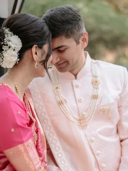 A close-up showing the bride's messy bun with flowers and the groom's pearl necklace, perfectly complementing their draped outfits.