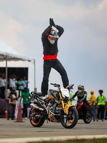 A stunt rider stands on their bike, clapping to energize the audience. The interaction between performers and the crowd is a key part of the Vroom experience.