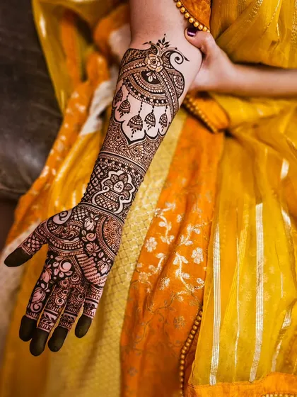 This design features elegant hanging jhumka motifs and a peacock, adding a touch of grace and movement to the bridal arm.