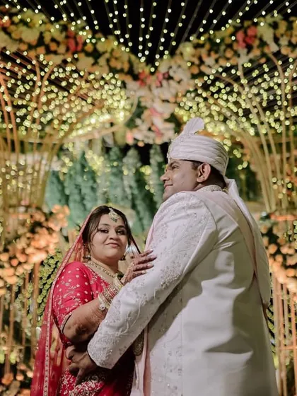 A candid shot of the couple at their wedding, with the magnificent, illuminated mandap creating a stunning and romantic backdrop.