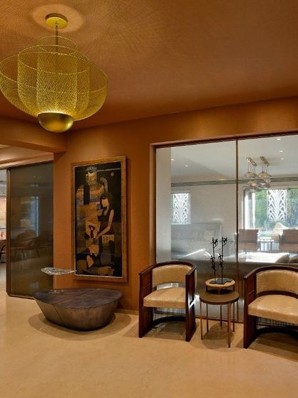 A cozy seating nook in a renovated home, defined by a warm, earthy color palette and a striking brass pendant light. Glass partitions maintain a sense of openness while creating distinct zones for different activities.