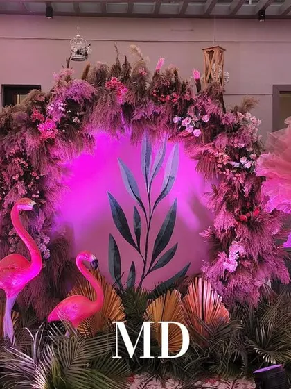 A creative photo point from a pastel-themed Mehendi ceremony. The backdrop features a mix of pampas grass and flowers, with neon pink flamingos adding a playful and modern touch.