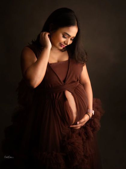 A quiet and intimate portrait. The mom-to-be looks down at her bump, her brown gown creating a soft, textured frame.