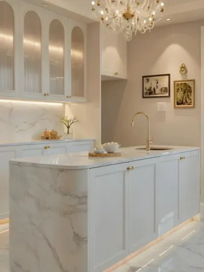 A classic and elegant all-white kitchen with a marble island. The gold hardware and beautiful chandelier add a touch of timeless glamour.