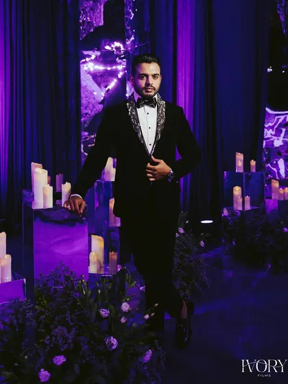 The groom, looking sharp and sophisticated in his tuxedo. The dramatic purple lighting and moody setting create a stylish and modern portrait.