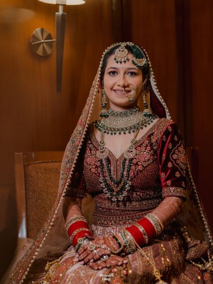 A classic seated bridal portrait, showcasing the bride's intricate jewelry and the rich velvet of her lehenga.