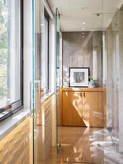 This office sundeck provides a space for relaxation and fresh air. The design uses glass panels and warm wood cabinetry to connect with the outdoors, while natural light floods the corridor.