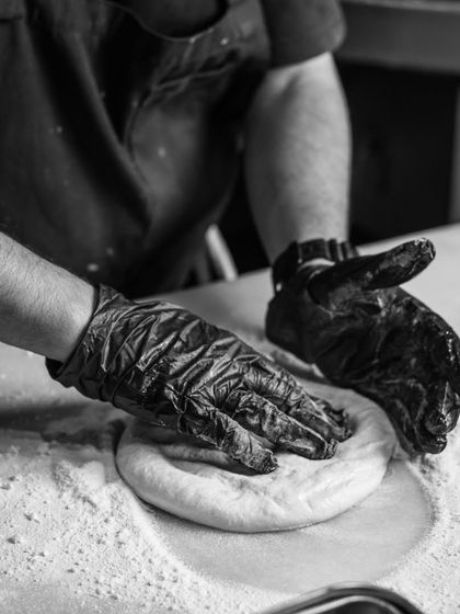 Behind the scenes. My hands, covered in flour, gently press and shape the pizza dough, the foundation of every great pizza.