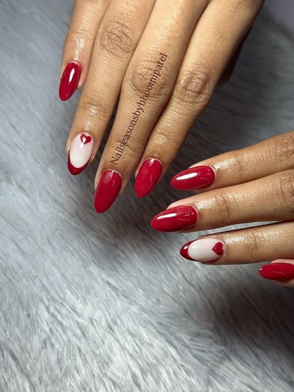 A classic red manicure with a cute twist. The accent nail features a negative space design with a tiny red heart.