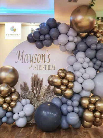 We specialize in modern and chic first birthday decorations. This stylish setup for 'Mayson's 1st Birthday' uses a sophisticated palette of matte grey, chrome gold, and dark blue balloons, complete with a personalized backdrop and pampas grass for a touch of elegance.