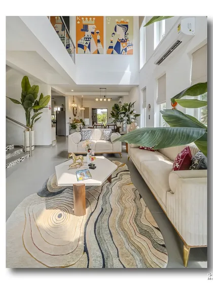A vertical composition of the double-height living area at Casa D Umravi in Goa. The shot emphasizes the room's scale, from the swirling patterns of the rug on the floor to the vibrant artwork that draws the eye upwards.