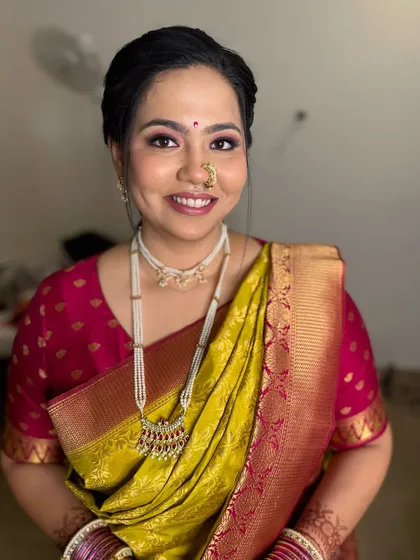 A lovely traditional look for this bride, featuring a classic bun, a Maharashtrian nath, and soft pink-toned makeup that complements her lime green and pink saree.