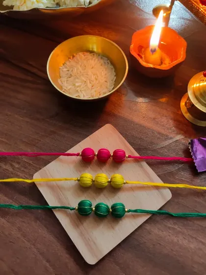 A set of colorful thread-bead rakhis. These are available in bright pink, yellow, and green, perfect for a festive celebration.