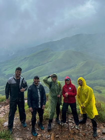 A small group of friends posing at a viewpoint on the Kudremukha trek, their colorful raincoats standing out against the misty green hills.